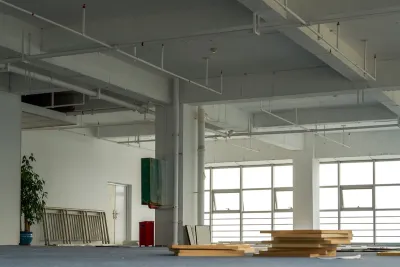 Vacant interior of open plan office with large buildings and stacked wood planks on floor.