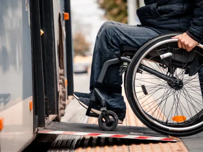 Close-up of person in wheelchair wearing jeans entering public bus on ramp.