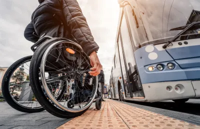 Ground-up view of man using wheelchair waiting to board a light blue bus.