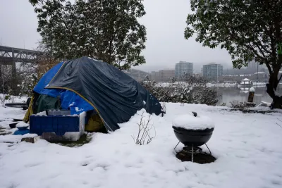 Blue tent with small charcoal grill and plastic bin set up by unhoused person in snow in Portland, Oregon.
