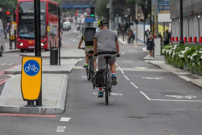 Protected two-way cycletrack on street in London, UK with red double-decker bus in background.