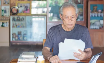 Gray-haired Asian man wearing glasses sitting at wooden table reading documents