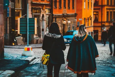 View from back of two women in winter clothing walking down street in European city.