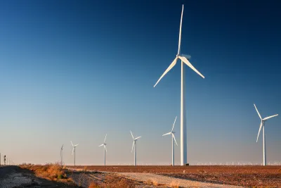 Row of white wind turbines in wide open dirt field in west Texas.