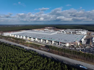 Birds-eye view of a large EV factory and nearby highway, all surrounded by forest.