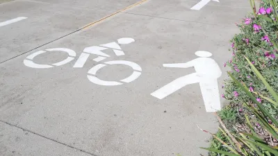 Close-up of white pedestrian and bike symbols painted on concrete path.
