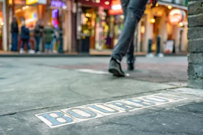 Low close-up of tile BOURBON sign in New Orleans street with pedestrian walking in background.