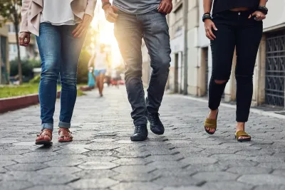 Close-up of bottom half of three people walking down city sidewalk paved with paving stones.