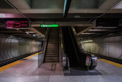 Empty underground Muni train platform in San Francisco with escalator, stairs in center of image.