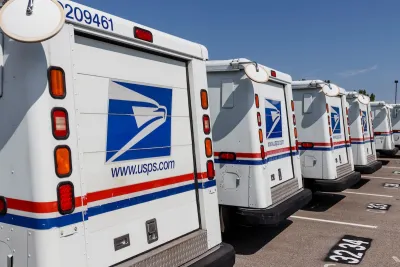 Row of USPS trucks parked in outdoor parking lot.