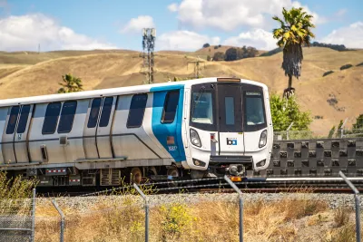 A white and blue Bay Area Rapid Transit (BART) train with golden hills and a palm tree in background.