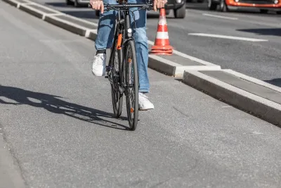 Close-up of person on road bike riding on protected bike lane separated by concrete curb from street.