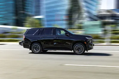 Large black SYV driving down city street with blurred background.