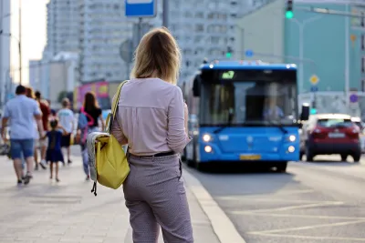 Woman waiting at city bus stop with blue bus pulling up.