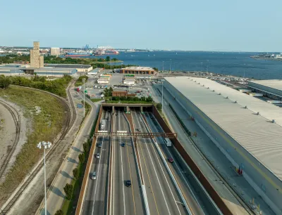 Aerial view of an eight-lane highway tunnel with the harbor in the background.