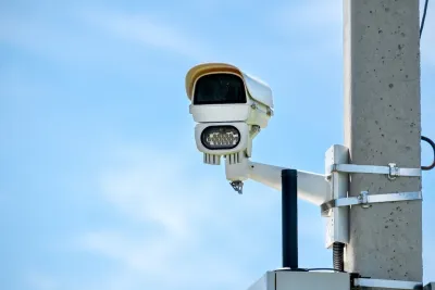 Close-up of white traffic enforcement camera mounted on concrete pole against blue sky.