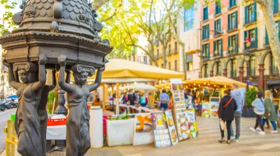Close-up of decorative water fountain on La Rambla pedestrian street in Barcelona, Spain with blurred pedestrians in background.
