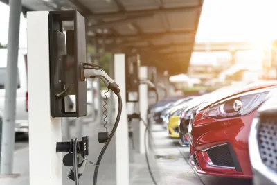 Close-up of red car parked and plugged in at EV charging station with row of cars behind it.