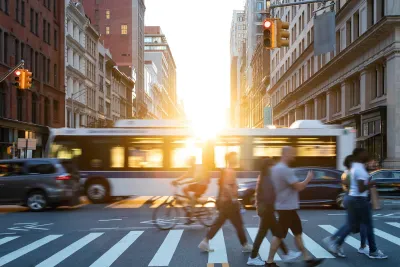 Pedestrians in a busy city intersection with a cirty bus passing behind them.