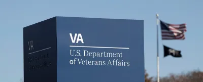 Close-up of Department of Veterans Affairs sign in Washington, D.C. with American and MIA flags on flagpole in background.