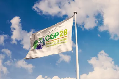 White flag with COP28 cliamte conference logo against lightly cloudy blue sky.