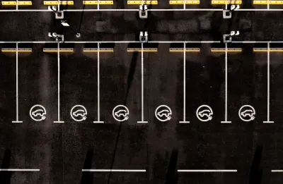 Overhead view of black asphalt parking lot with white lined parking spots with EV charging logos.