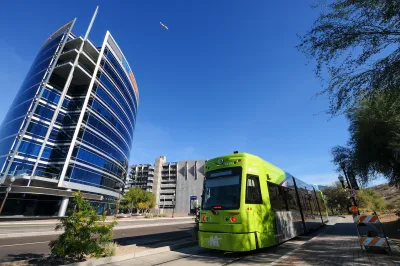 Green Tempe streetcar with downtown Tempe glass building in background.