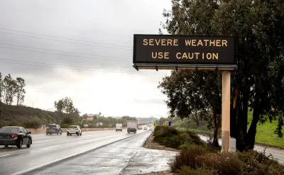 Freeway sign with "severe weather - use caution" over multilane freeway in rainy weather.
