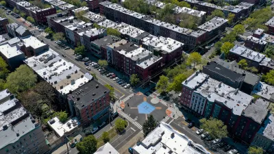 Aerial view of intersection in Hoboken, New Jersey with crosswalks, bulb-outs, and blue home plate painted in middle of intersection, surrounded by mid-rise multistory apartment buildings.