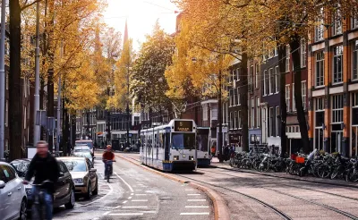 Tram and cyclist on Amsterdam street with sunrise or sunset in background.
