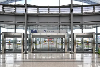 View of large glass building with glass doors and "To Trains" sign.