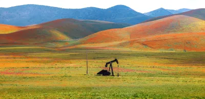 Abandoned oil well against hill covered in blooming orange flowers in Carrizo Plain National Monument, California.