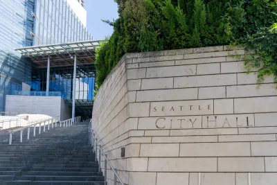 Close-up of engraved stone Seattle City Hall sign in front of wide steps leading to modern glass building.