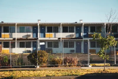 Closed, boarded-up two-story motel behind chain-link fence.