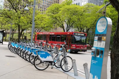 Blue and white Pittsburgh bike share bikes lined up at a station with a red city bus on street in background.