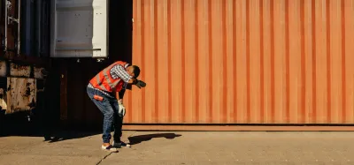 Worker in safety vest leaning over expressing heat exhaustion standing next to orange shipping container.