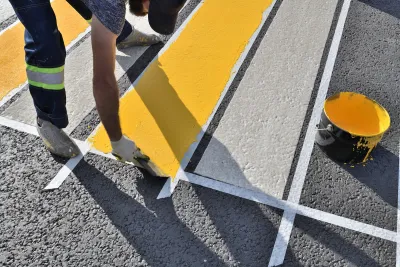 Close-up of man painting white and yellow crosswalk on asphalt.