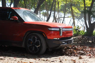 Red Rivian electric truck on forested beach in the Dominican Republic.