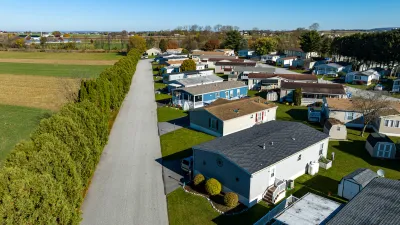 Aerial view of mobile home community in rural area with homes lined up diagonally next to small road.