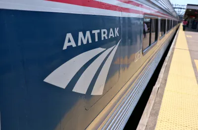 Close-up of Amtrak logo on blue passenger train stopped at outdoor station platform.
