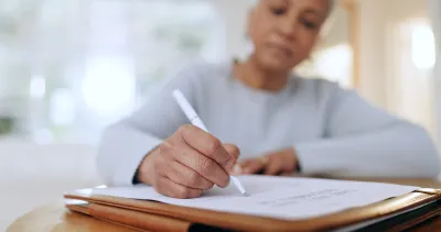 Older black woman writes on document with a pen.