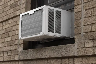 Close-up of white air conditioning window unit in window of brown brick building.