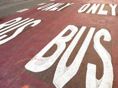 White BUS ONLY letters on red painted bus lane on street.
