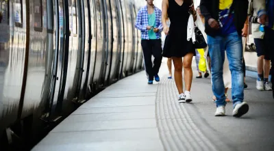 Low shot of side of subway or commuter train and passengers walking on platform next to it.