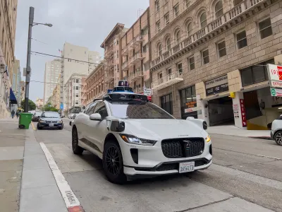White Waymo self-driving taxi on street in San Francisco, California with brick buildings in background.