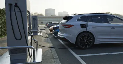 Row of vehicles parked and plugged in at EV charging station.