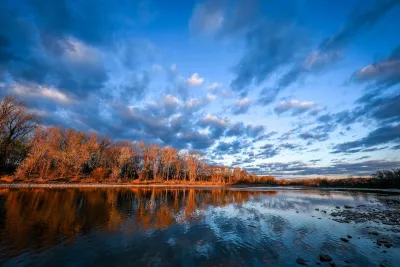 View of calm Maumee River with fall foliage on other side at sunset.