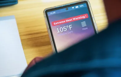 Close-up over shoulder of person holding smartphone with extreme heat warning and 105 degree temperature indicated.