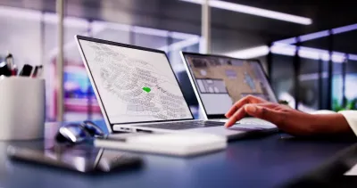 Close-up of laptop with GIS parcel map open and hand resting on keyboard in modern office.