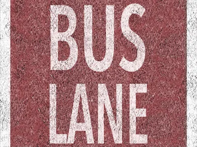 Overhead view of white BUS LANE sign painted on red background on concrete street.